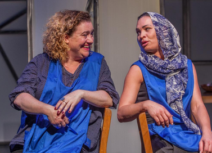 Photo of two women, both wearing blue aprons, sitting down facing each other
