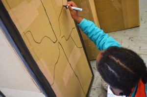 Child drawing a pattern on a large piece of cardboard with black marker pen