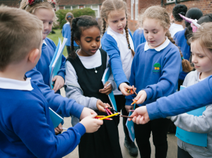 Schoolchildren participating in A Small Tale - Punchdrunk and Z-arts. Several schoolchildren are standing in a circle, they are all holding coloured pencil crayons and putting their hands into the centre of the circle