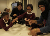 Picture of schoolchildren and teachers constructing a shape out of white marshmallows and wooden sticks.