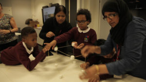 Picture of schoolchildren and teachers constructing a shape out of white marshmallows and wooden sticks.