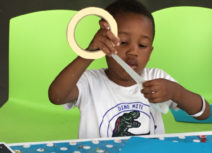 Young boy sitting on a lime green chair holding a roll of masking tape and wearing a white t-shirt
