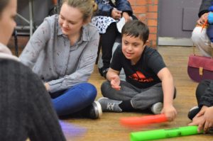 A woman wearing a black and white striped tshirt is sat next to a boy wearing a black tshirt with a red 'Adidas' logo. They are both holding colourful tubes.