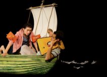 Adrift production photo. A young girl and a young boy in a boat with a sail. They are both wearing arm bands or a life jacket.