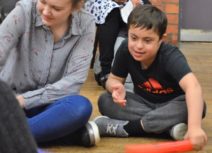 A woman wearing a black and white striped tshirt is sat next to a boy wearing a black tshirt with a red 'Adidas' logo. They are both holding colourful tubes.