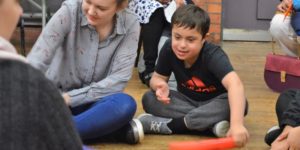 A woman wearing a black and white striped tshirt is sat next to a boy wearing a black tshirt with a red 'Adidas' logo. They are both holding colourful tubes.