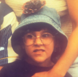 Photo of young girl wearing round glasses and a denim fisherman's hat with a flower on the front