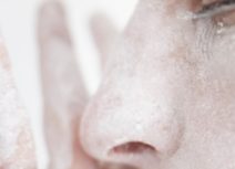 Close up of face, side on, with a hand next to it. Both covered in chalk.