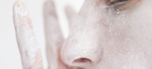 Close up of face, side on, with a hand next to it. Both covered in chalk.