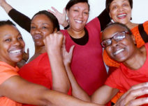 Five women wearing red tops. They are all looking at the camera, smiling and waving their arms