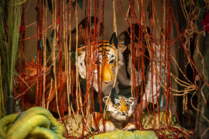Two tiger puppet faces behind jungle vines