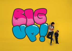 Production image for 'Big Up!'. The word 'Big' is written in large pink cartoon bubble writing and the word 'up!' is written below it in the same font but in blue. A teenage girl is leaning against the exclamation mark at the end of the word 'up' looking down at a younger, shorter boy.
