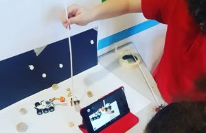 Promotional image for Digital Discoverers - photo from a workshop. Two children are doing stop motion animation - they are recording using a tablet, the scene they have created is a scene on the moon with a spaceman and a space buggy