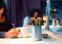 Photo of woman sitting at a table drawing with coloured pencils