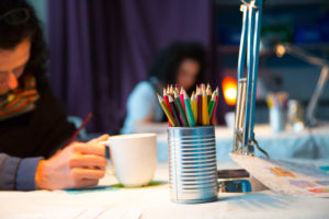 Photo of woman sitting at a table drawing with coloured pencils