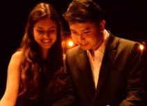 Picture of a man and woman sat together dressed in formal wear. They are looking down and towards the left