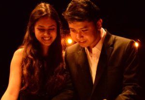 Picture of a man and woman sat together dressed in formal wear. They are looking down and towards the left