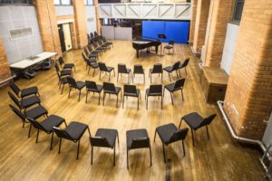 Photo of three rows of black chairs in a horseshoe shape facing a grand piano