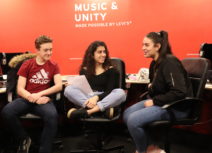 Promo image - Arts and Culture for Teenagers in Manchester - Family Workshop. Two teenage girls and a teenage boy are sat in a room with red painted walls, they are smiling and talking to each other