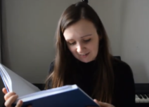 Photo of a young woman reading from a large blue book. The story is Alice in Wonderland.