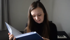 Photo of a young woman reading from a large blue book. The story is Alice in Wonderland.
