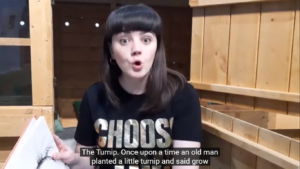 Lead image for story time with Alice - photo of a young woman with dark hair and a fringe holding a book and looking at the camera