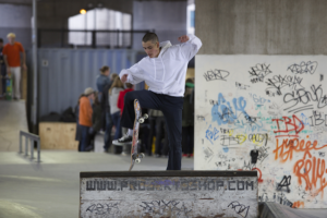 Man in white hoodie making a jump on a skateboard from a ramp