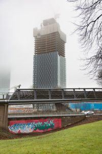 Photo of one of the Deansgate Square buildings in construction, a motorway footbridge is in the foreground.
