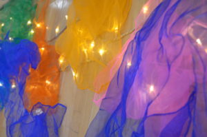 A close up photo of different coloured sheets of mesh hanging in front of white fairy lights.
