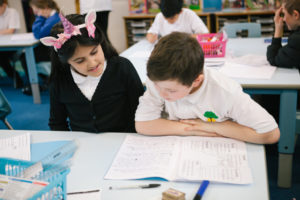 A young girl and a young boy working together, looking at a creative writing book