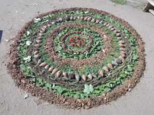 photo of a mandala pattern on the ground made from natural materials including rocks, soil and leaves